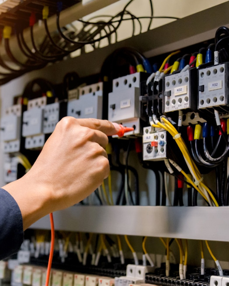 Electrician using a probe to test connections in an electrical control panel with labeled switches and colored wires